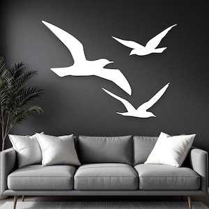 Puede incluir: Tres siluetas de aves blancas en vuelo dispuestas en grupo sobre una pared gris oscuro. Las aves est&aacute;n representadas con las alas extendidas en posici&oacute;n de planeo, creando un alto contraste visual sobre el fondo oscuro y s&oacute;lido.