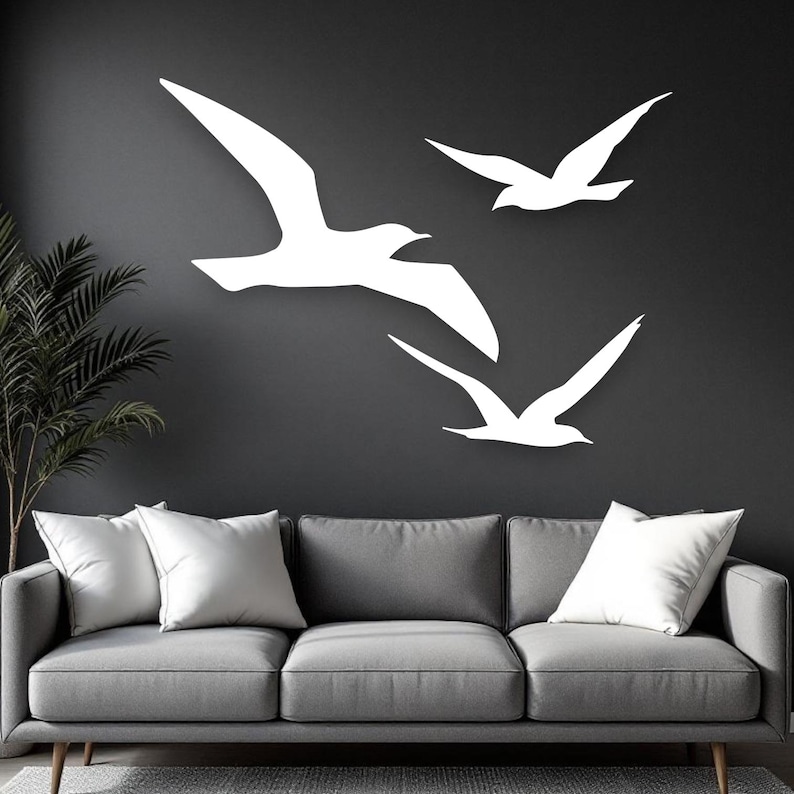 Puede incluir: Tres siluetas de aves blancas en vuelo dispuestas en grupo sobre una pared gris oscuro. Las aves est&aacute;n representadas con las alas extendidas en posici&oacute;n de planeo, creando un alto contraste visual sobre el fondo oscuro y s&oacute;lido.