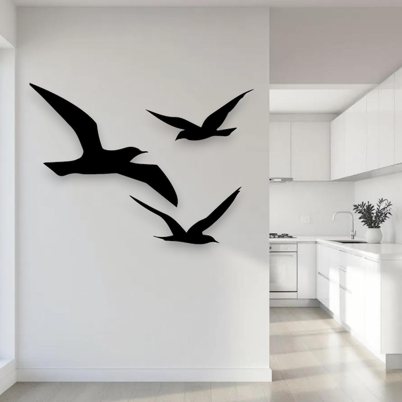 Puede incluir: Un conjunto de tres siluetas de aves negras montadas en la pared en pleno vuelo. El dise&ntilde;o presenta un ave grande a la izquierda con las alas extendidas y dos aves m&aacute;s peque&ntilde;as a la derecha, una sobre la otra, todas en un color negro s&oacute;lido.
