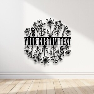 Puede incluir: Arte mural floral de metal negro con el texto "YOUR CUSTOM TEXT" en el centro. El dise&ntilde;o presenta varias flores y hojas dispuestas en forma circular, adecuado para la decoraci&oacute;n del hogar.