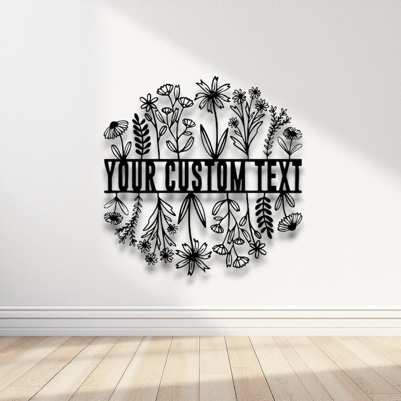 Puede incluir: Arte mural floral de metal negro con el texto "YOUR CUSTOM TEXT" en el centro. El dise&ntilde;o presenta varias flores y hojas dispuestas en forma circular, adecuado para la decoraci&oacute;n del hogar.