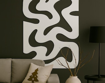 Könnte beinhalten: Ein großes, weißes, abstraktes Wandkunstwerk mit einem fließenden, organischen Design ist an einer dunklen Wand angebracht. Das Kunstwerk ist rechteckig mit ausgeschnittenen Formen. Ein graues Sofa mit einem dekorativen Kissen und eine schwarze Lampe befinden sich im Vordergrund.