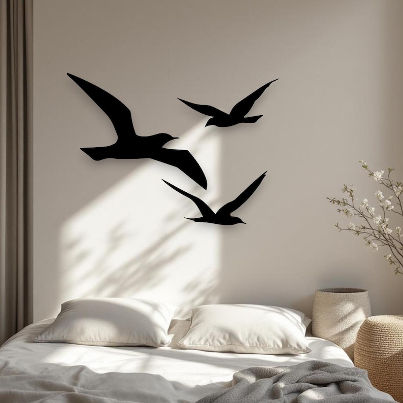 Puede incluir: Un conjunto de tres siluetas de aves negras montadas en una pared. Las aves se representan en vuelo con las alas extendidas, dispuestas en una formaci&oacute;n escalonada. El ave m&aacute;s grande est&aacute; a la izquierda, con dos m&aacute;s peque&ntilde;as a la derecha.