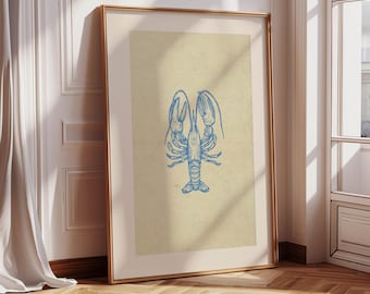May include: A framed art print featuring a blue lobster illustration on a beige background. The artwork is displayed in a gold frame and leans against a white wall. The print is a vertical rectangle, showcasing the lobster's detailed outline.