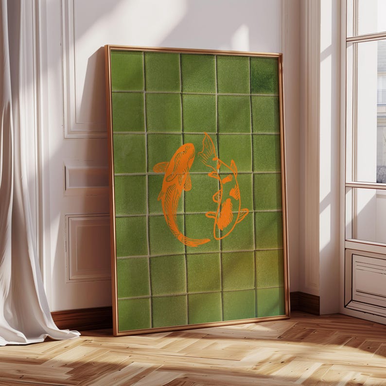 May include: A framed artwork featuring a green tiled background with two orange koi fish. The artwork has a gold frame and is leaning against a white wall. The image is well-lit, showcasing the details of the fish and tiles.