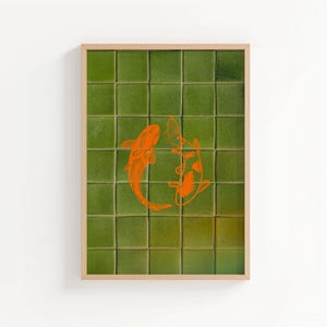 May include: Framed art print featuring two orange koi fish swimming in a circle. The background is a grid of green square tiles. The frame is a light wood color. The artwork is displayed on a white wall.