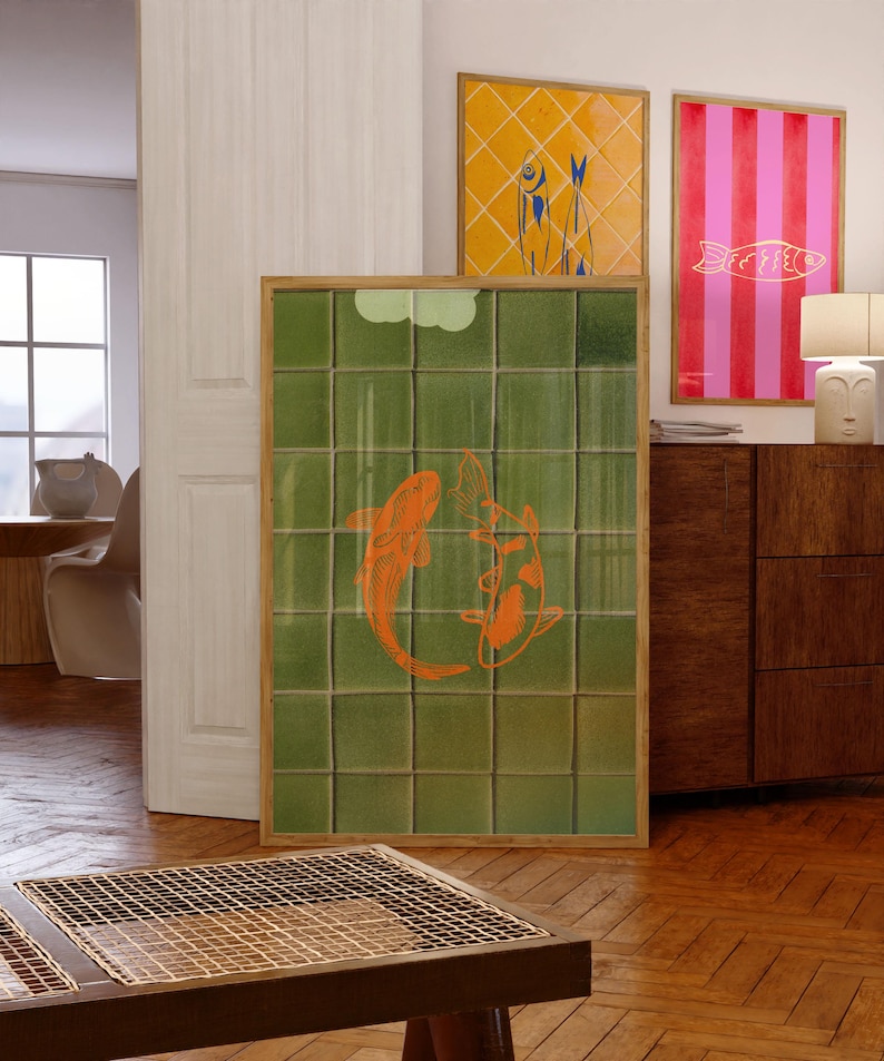 May include: A framed artwork featuring two orange koi fish on a green tiled background. Two additional framed artworks are visible, one with a yellow diamond pattern and blue fish, and another with pink and red stripes and a gold fish.