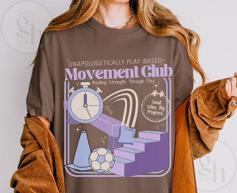May include: Brown t-shirt with a graphic design featuring a stopwatch, stairs, a soccer ball, and the text "UNAPOLOGETICALLY PLAY-BASED Movement Club Building Strength Through Play." The design includes purple, blue, and white elements.