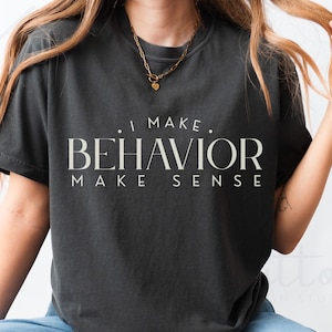 Peut inclure: T-shirt gris foncé avec l'inscription "I MAKE BEHAVIOR MAKE SENSE" en police serif. Le t-shirt est de style col rond et semble être fait d'une matière douce et confortable. Le t-shirt est de style décontracté.