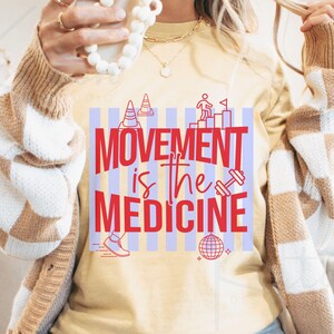 May include: A light yellow t-shirt with the text "MOVEMENT is the MEDICINE" in red. The shirt features graphics of a dumbbell, a running shoe, a disco ball, and other fitness-related icons. The shirt is part of a fitness or wellness collection.
