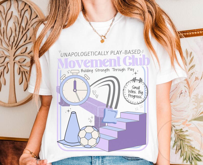 May include: White t-shirt with a graphic design featuring the text "UNAPOLOGETICALLY PLAY-BASED Movement Club Building Strength Through Play." The design includes a stopwatch, stairs, a soccer ball, and the phrase "Small Wins. Big Progress."