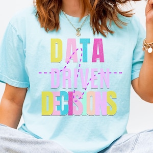 May include: Light blue t-shirt with the text "DATA DRIVEN DECISIONS" in colorful block letters. The text is in yellow, pink, blue, and purple. The shirt has short sleeves and a crew neck.