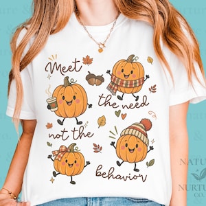 Op de afbeelding: Een wit T-shirt met korte mouwen en een afbeelding van vier cartoonpompoenen met gezichten. De tekst luidt Meet the need not the behavior. De pompoenen zijn versierd met een koffiebeker, een sjaal, een strik en een gebreide muts.