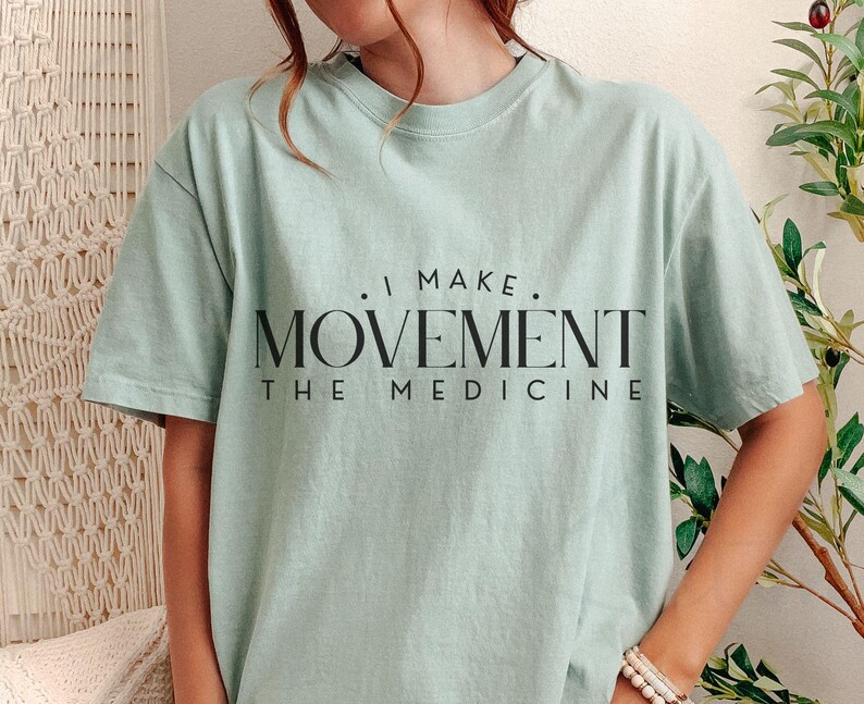 May include: A light green t-shirt with the text ". I MAKE. MOVEMENT THE MEDICINE" in black. The shirt has short sleeves and a crew neck. The shirt is made of a soft material.