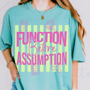 Pode incluir: Camiseta turquesa com as palavras rosa "FUNCTION Before ASSUMPTION" em um fundo de listras verticais verde limão. A camiseta apresenta ícones gráficos de uma xícara de café, lupa, lista de verificação e estrelas.