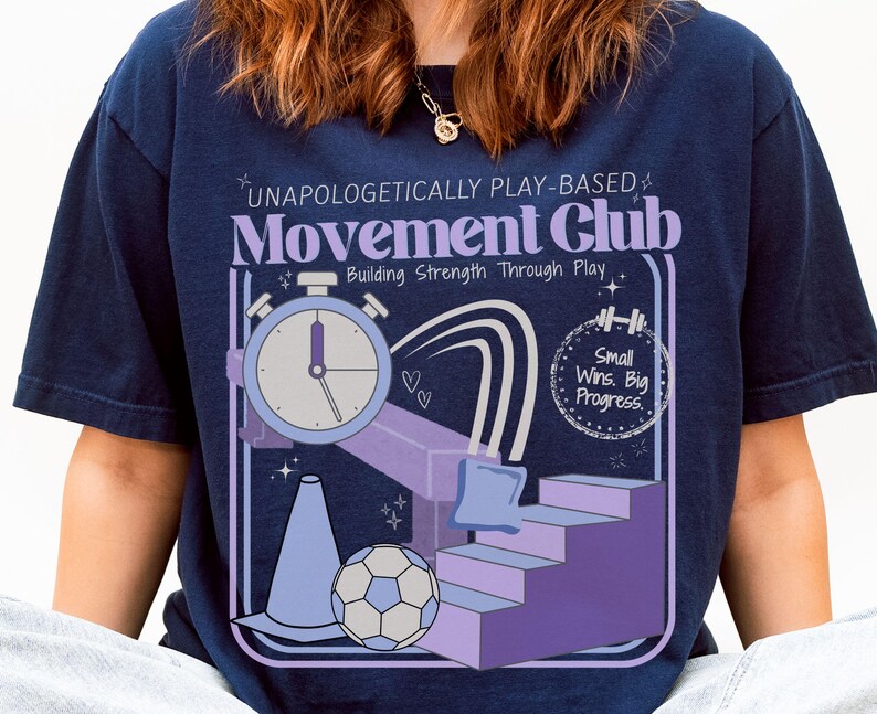 May include: Navy blue t-shirt with a graphic design for a Movement Club. The design includes a stopwatch, a soccer ball, a cone, and the text "UNAPOLOGETICALLY PLAY-BASED Movement Club Building Strength Through Play Small Wins. Big Progress."