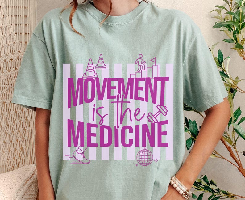 May include: A light green t-shirt with the text "MOVEMENT is the MEDICINE" in bright pink. The design includes illustrations of traffic cones, a person climbing stairs, a dumbbell, a running shoe, and a disco ball.
