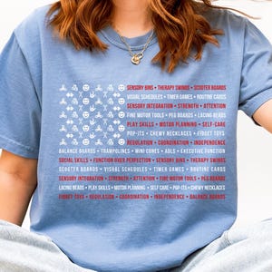 Könnte beinhalten: Ein hellblaues T-Shirt mit einem grafischen Design, das der amerikanischen Flagge ähnelt, mit einem weißen Feld mit verschiedenen Symbolen und roten Streifen mit Text. Der Text enthält Begriffe wie "Sensory Bins", "Play Skills" und "Fidget Toys".