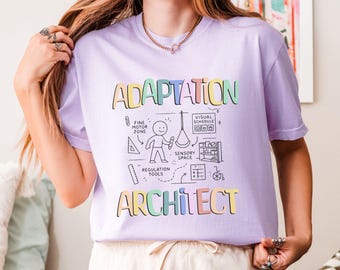 May include: A lilac t-shirt with the words "ADAPTATION ARCHITECT" in colourful, outlined letters. The shirt features black and white illustrations of educational tools and a stick figure. The shirt is made of a soft material.