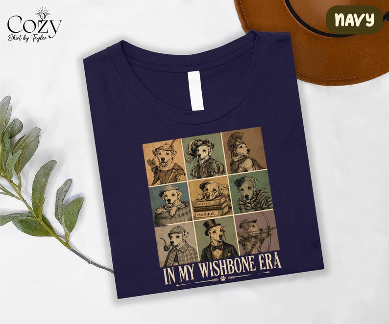 a navy blue t-shirt with a graphic design of nine dog illustrations arranged in a 3x3 grid, each depicting a different dog character. The text "IN MY WISHBONE ERA" is printed below the image.