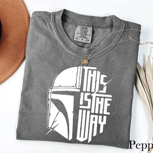 a gray t-shirt with a graphic design, a brown hat, and some dried leaves, all placed on a white surface.