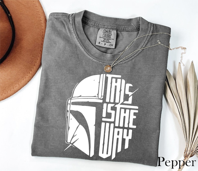 a gray t-shirt with a graphic design, a brown hat, and some dried leaves, all placed on a white surface.