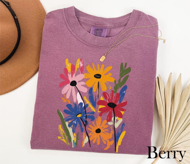 a purple t-shirt with a colorful floral design, a brown hat, and a fan, all arranged on a white background.