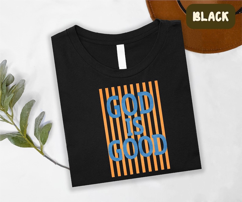 A black t-shirt with the text "GOD IS GOOD" printed on it, along with orange and blue vertical stripes.