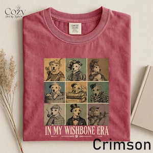 A pink t-shirt with a collage of nine illustrations of dogs in various poses and outfits, along with the text "IN MY WISH BONE ERA" and "Crimson" printed on it.