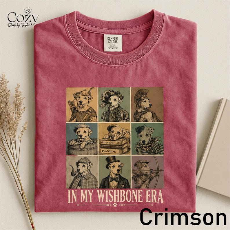 A pink t-shirt with a collage of nine illustrations of dogs in various poses and outfits, along with the text "IN MY WISH BONE ERA" and "Crimson" printed on it.