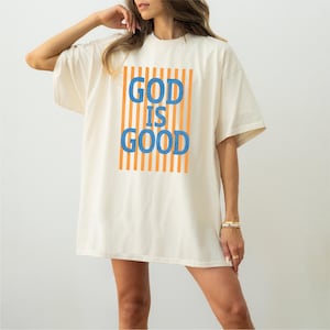 A woman wearing a white t-shirt with the text "GOOD IS GOOD" printed on it.