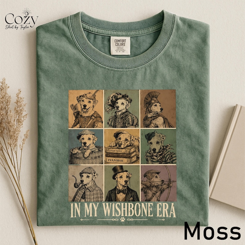 A green t-shirt with a collage of nine different dog illustrations, each with a unique pose and expression, arranged in a grid pattern. The text "IN MY WISHbone ERA" is printed below the collage.