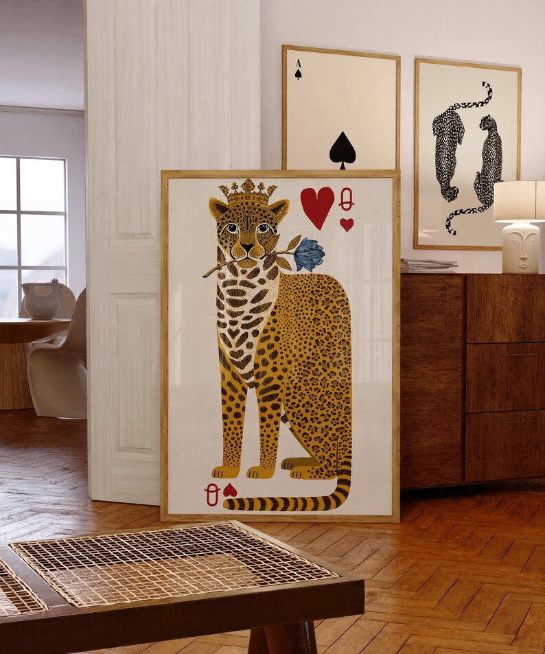 May include: A framed art print featuring a leopard wearing a crown and holding a blue rose, with playing card symbols. The leopard has a yellow and brown spotted coat. Additional framed art pieces are visible in the background.