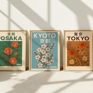 以下が含まれることがあります： 日本の都市名と花のイラストが描かれた、ヴィンテージ風のポスター3枚。ポスターは金色で額装されており、薄い青、緑、ベージュの背景になっています。ポスターには「大阪」、「京都」、「東京」の文字と、2020年と1997年の年号が書かれています。