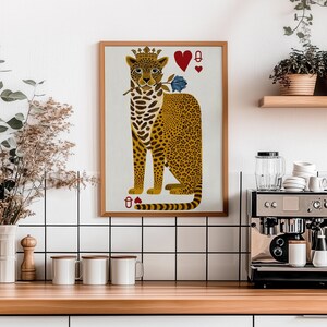 May include: A framed art print featuring a leopard wearing a crown and holding a blue rose. The leopard is depicted as the Queen of Hearts playing card. The print has a wooden frame and is displayed in a kitchen setting.