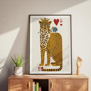May include: A framed art print featuring a stylized leopard wearing a crown and holding a blue rose. The leopard has a spotted coat and is depicted with playing card symbols, including the Queen of Hearts. The artwork is displayed on a wooden cabinet.