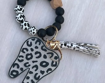 May include: Black and white leopard print tooth charm keychain with a black beaded bracelet and a wooden bead.