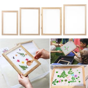 May include: A set of four rectangular wooden paper making frames with mesh screens. The frames are shown in use with a wooden spoon to arrange pressed flowers and green leaves onto wet paper pulp within the mesh screen for crafting.