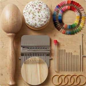 May include: A darning loom kit featuring a wooden mushroom-shaped darning tool, a floral fabric pincushion, a circular organizer with multi-colored embroidery threads, a metal darning loom, a clear needle tube, various sewing needles, and five wooden rings.