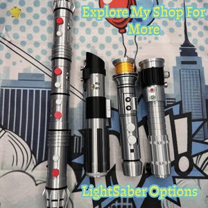 Może przedstawiać: Wyświetlane są cztery srebrne miecze świetlne z czerwonymi i białymi przyciskami oraz czarnymi akcentami. Obraz zawiera tekst "Explore My Shop For More" i "LightSaber Options" z "More To Come!!!" na dole.