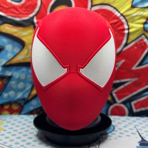 May include: A red Spider-Man mask with white eye details and a black base. The mask has a textured surface and is displayed against a colorful comic book-style background. Text on the image reads "Check Out My Store" and "For Other SpiderMan Variations."