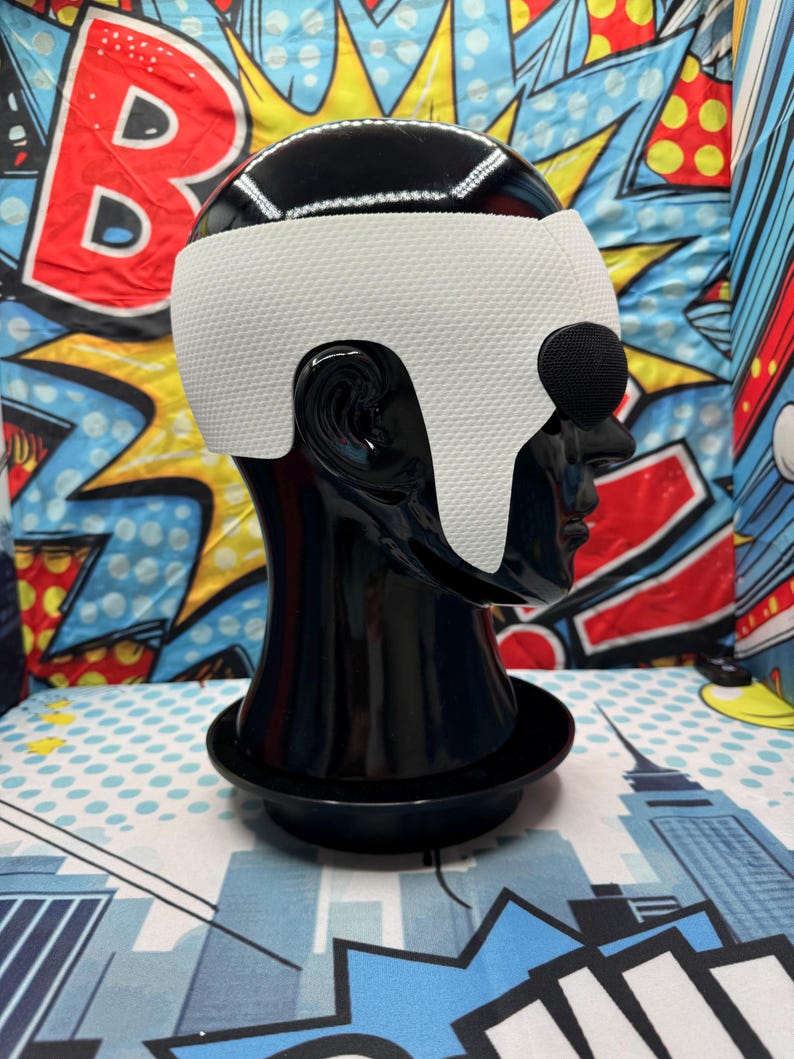 Puede incluir: Una cabeza de maniqu&iacute; negra con una cubierta para la cabeza blanca y negra. La cubierta para la cabeza tiene una banda blanca en la frente y alrededor de las orejas. El fondo es un dise&ntilde;o de arte pop colorido.