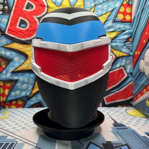 May include: A futuristic-style mask with a black base and a red mesh visor. The mask features a blue forehead section and white trim. The design is reminiscent of a superhero or sci-fi character.