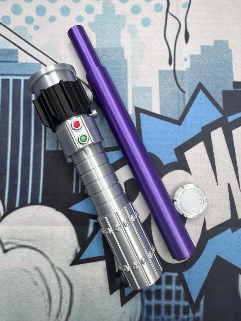 Puede incluir: Un sable de luz plateado y negro con botones rojos y verdes, un mango morado y una tapa plateada. El sable de luz est&aacute; sobre un fondo azul y blanco estilo c&oacute;mic.