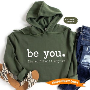 May include: A green hooded sweatshirt with the text "be you. The world will adjust" in white lettering.