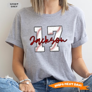 May include: Gray t-shirt with a baseball-themed design featuring the number 17 and the name "Jackson" in red.