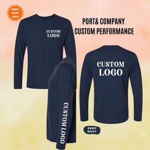 May include: A deep navy long-sleeve performance shirt by Port & Company. The shirt is shown from the front, back, and side, featuring the white text CUSTOM LOGO on the left chest, the back, and vertically along the right sleeve. The text PORT & COMPANY CUSTOM PERFORMANCE is visible.