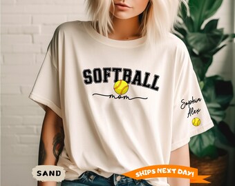 May include: Sand-colored t-shirt with the words "SOFTBALL mom" in black and a yellow softball graphic. The name "Sophia Alex" is written on the sleeve, along with a small softball graphic.