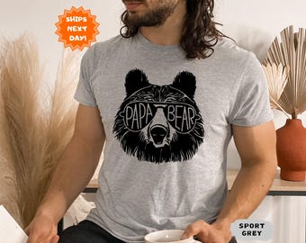 May include: Sport grey t-shirt featuring a black graphic of a bear wearing sunglasses with the text "PAPA BEAR" in the lenses. The shirt is a short-sleeved crew neck. The image also includes a "SHIPS NEXT DAY!" sticker.