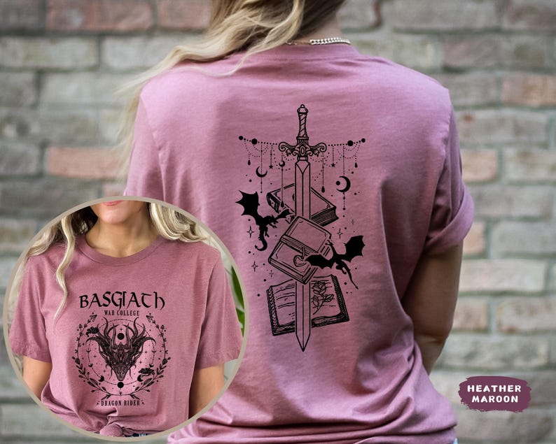 May include: Heather maroon t-shirt with a black graphic on the back featuring a sword, books, bats, and celestial elements. The front of the shirt has a circular design with text and a dragon illustration. The shirt is a crew neck.